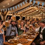 People in dirndls and lederhosen raising beer steins inside a Bavarian Oktoberfest tent