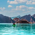 Kayaker paddling on the turquoise water of Hatta Dam with the Hajar Mountains behind