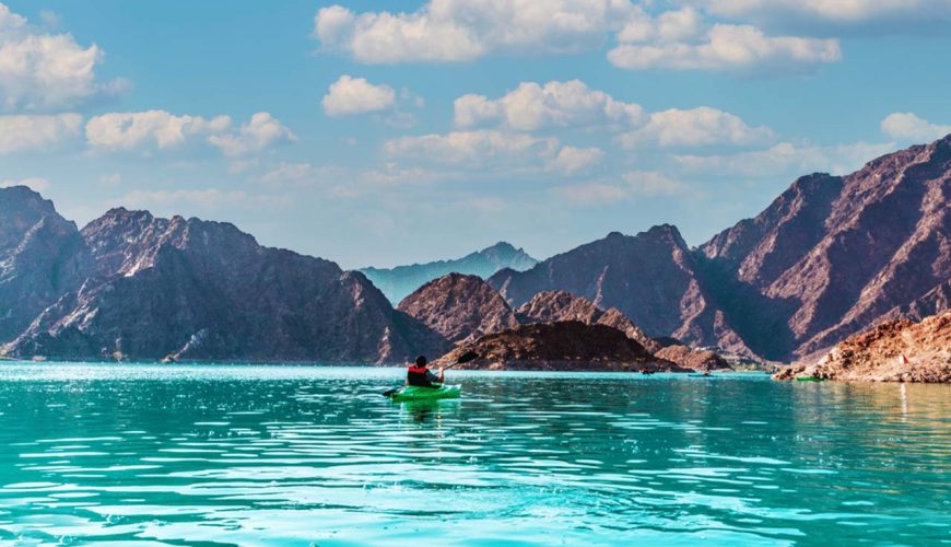 Kayaker paddling on the turquoise water of Hatta Dam with the Hajar Mountains behind