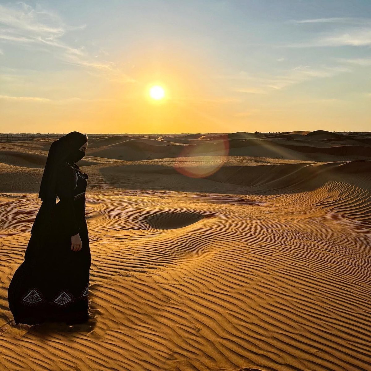 Woman in a classic black closed abaya silhouetted in the Dubai desert at sunset
