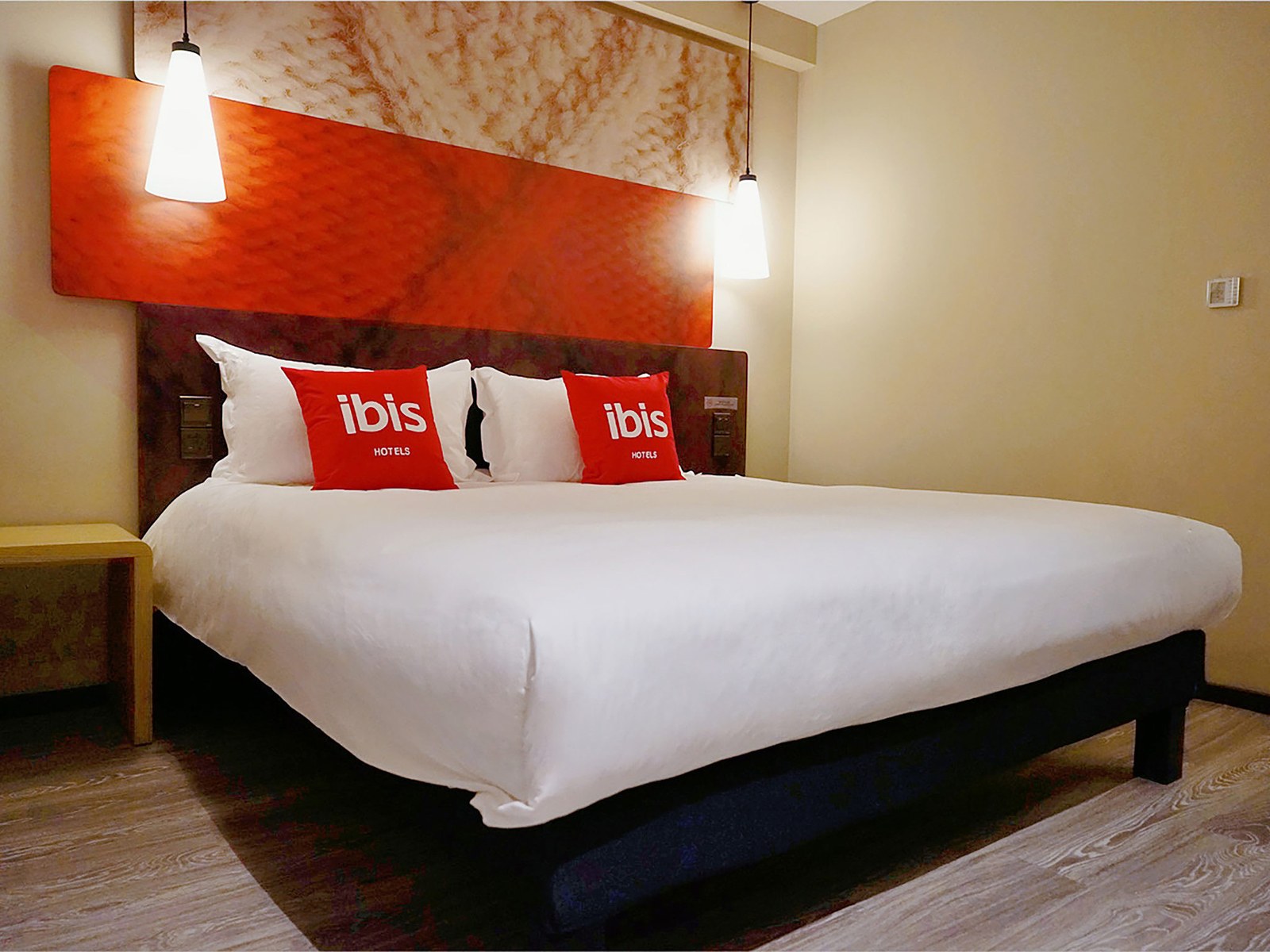 Crisp white bed with red ibis cushions in a modern ibis hotel room