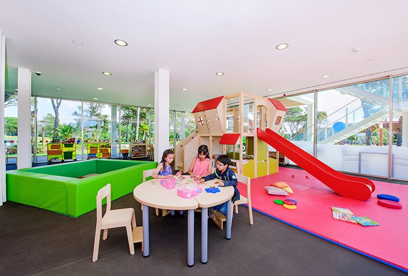 Children playing at a bright hotel kids club with slide and activity tables
