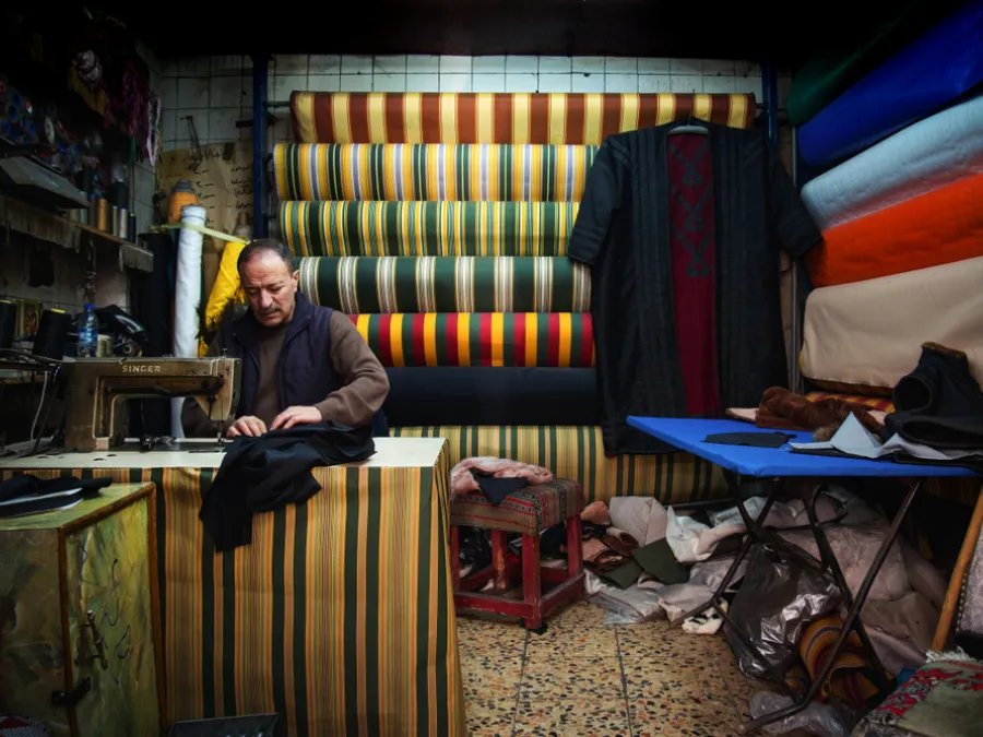 A tailor sewing garments inside a traditional fabric shop in old Dubai
