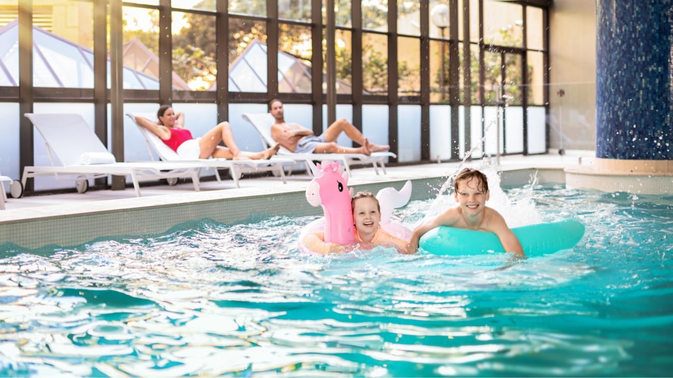 Children playing with inflatables in a hotel pool while parents relax nearby