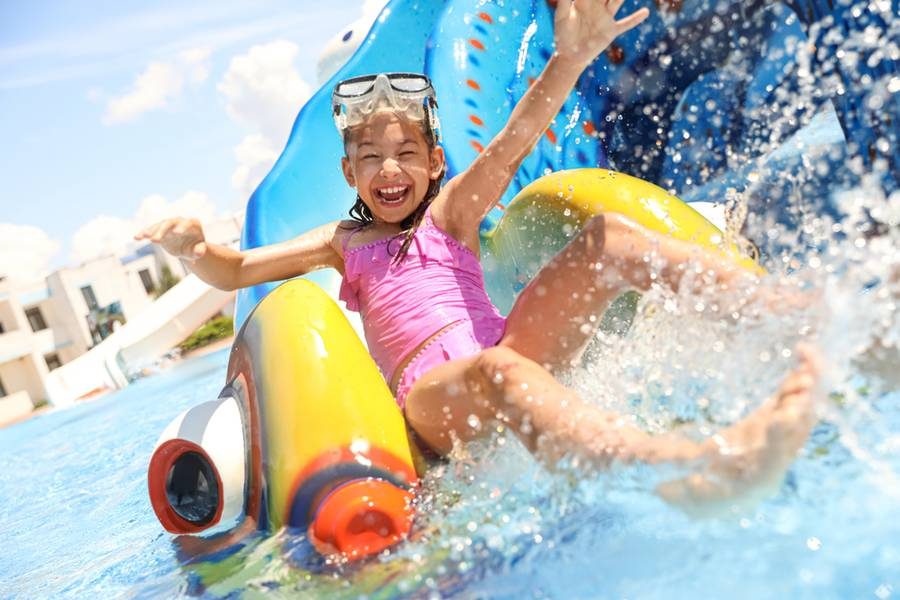Young child splashing down a colorful hotel waterslide in the sun