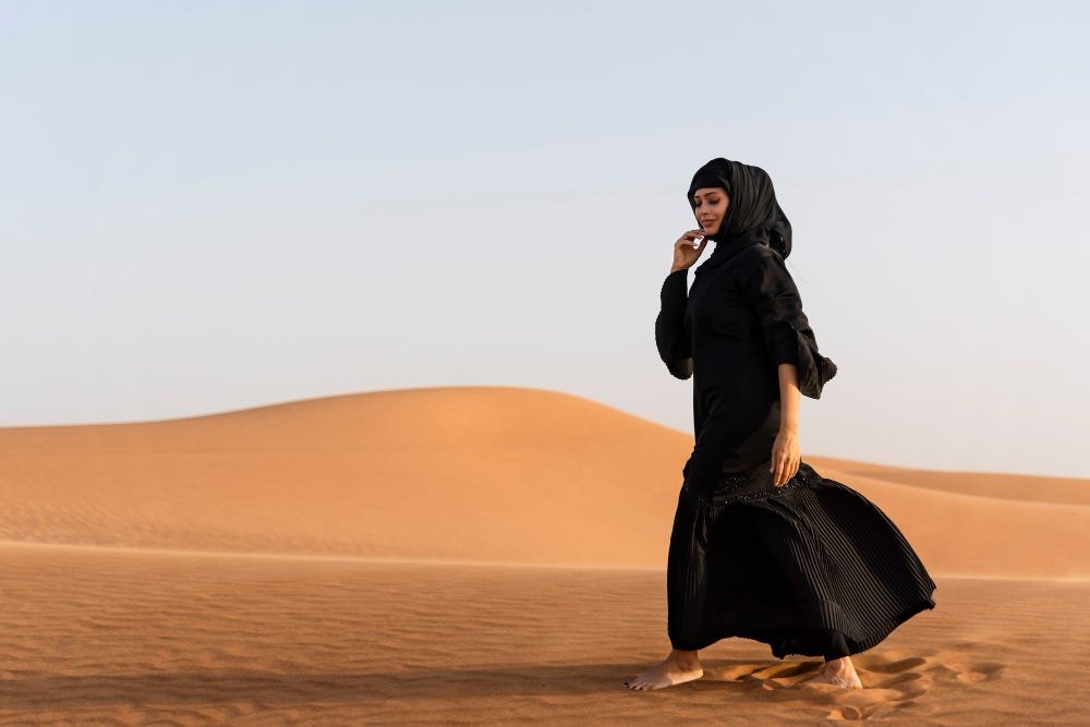 Woman in a black abaya walking across Dubai desert dunes