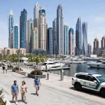 Tourists walking along the Dubai Marina promenade with a Dubai Police patrol car nearby