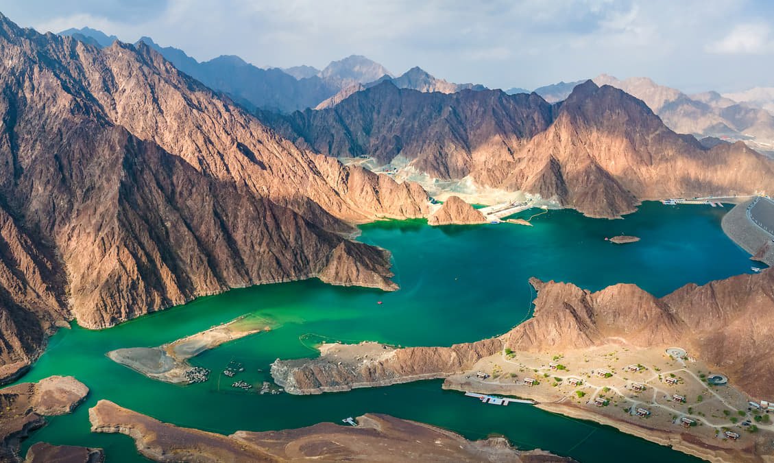 Aerial view of Hatta Dam's green-blue reservoir surrounded by Hajar Mountains
