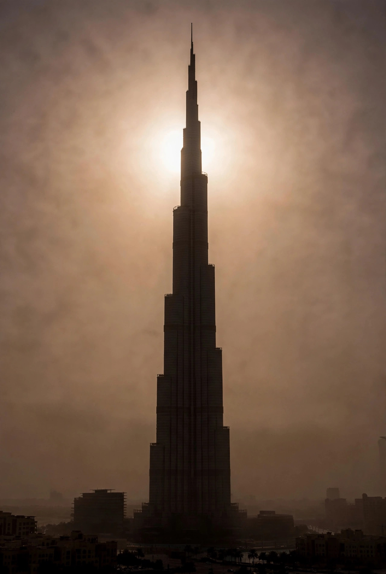 Hazy sun glowing behind the silhouette of the Burj Khalifa under a dusty sky