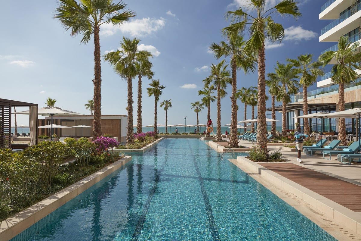 Contemporary resort pool lined with cabanas leading towards the beach in Jumeirah