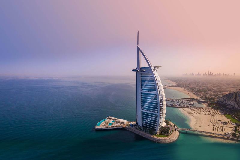 Sail-shaped hotel tower rising from its own island against the Dubai skyline