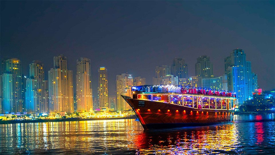 An illuminated dhow cruise boat sailing past Dubai Marina's towers at night