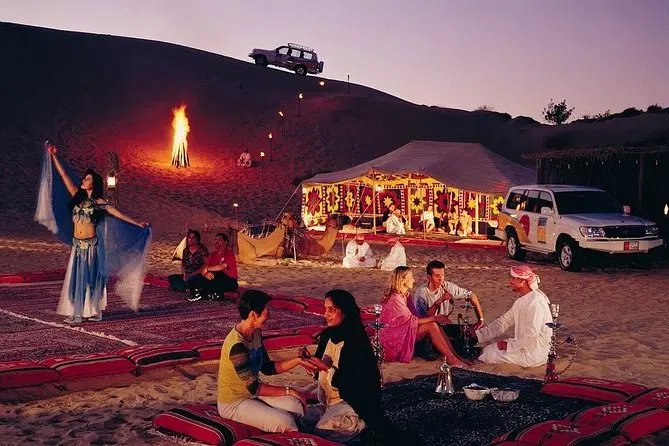 Guests enjoying an evening desert safari camp in Dubai with traditional dancing, a bonfire and low seating around the dunes