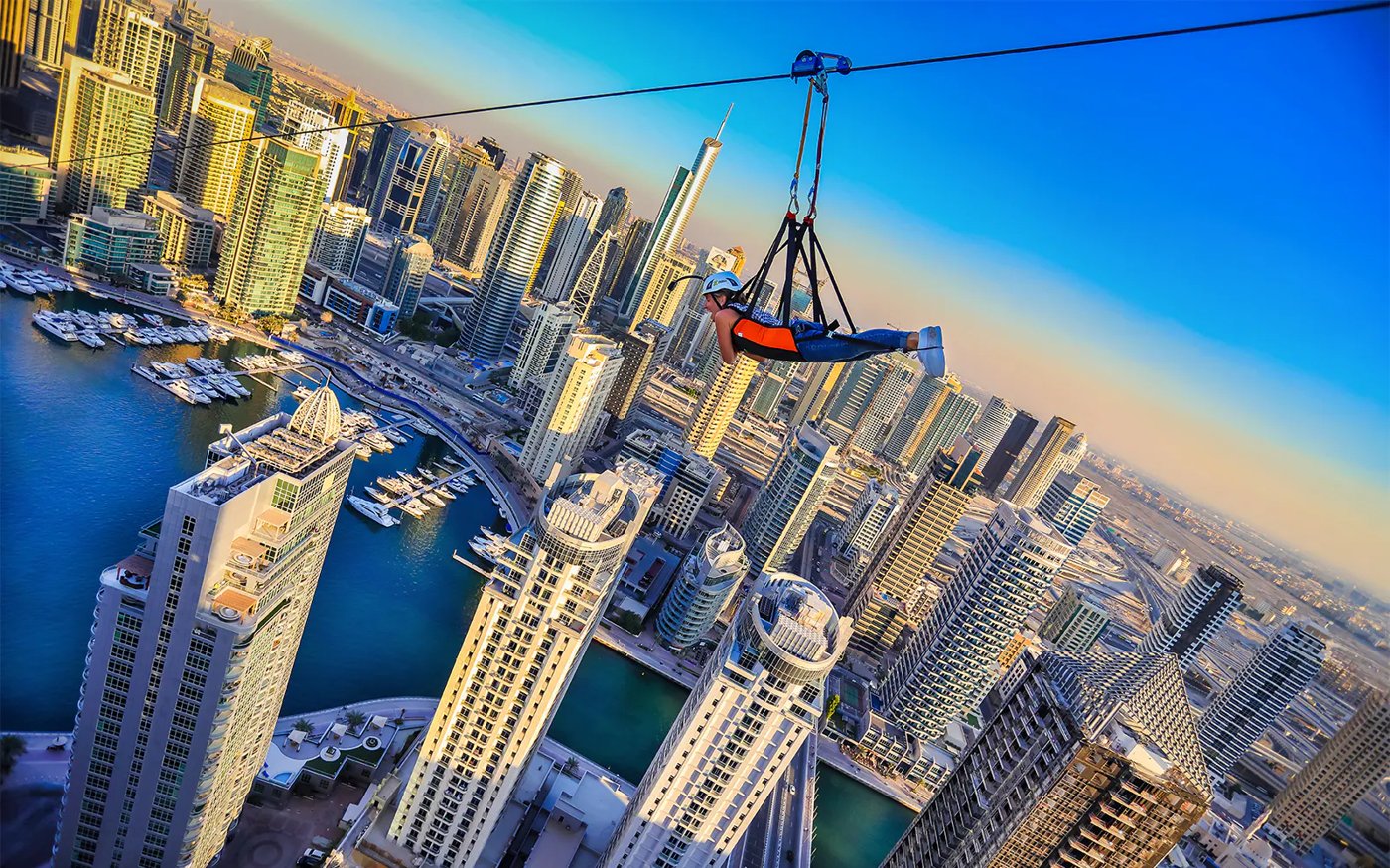 Person riding a zipline between Dubai Marina towers above the water