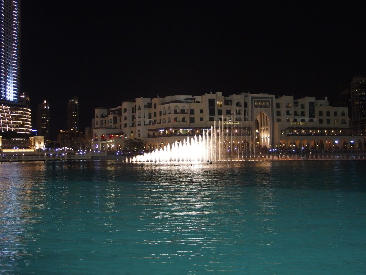 The Dubai Fountain lit up at night in front of Souk Al Bahar