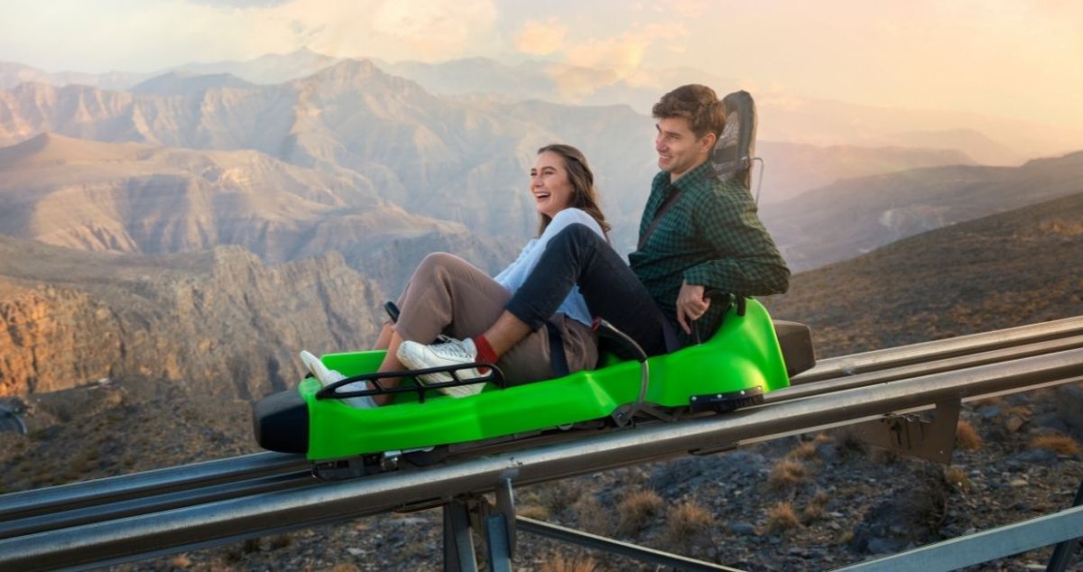 Couple riding a green alpine toboggan sled on the Jais Sledder track with mountain views