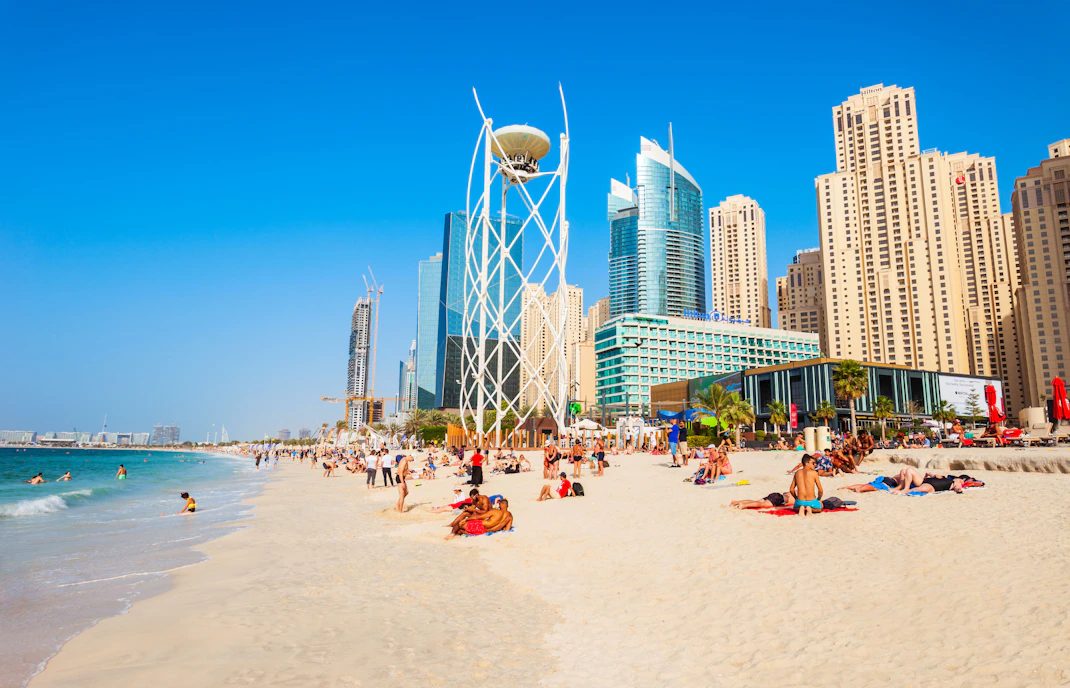 People swimming and relaxing at JBR beach with the Marina skyline behind