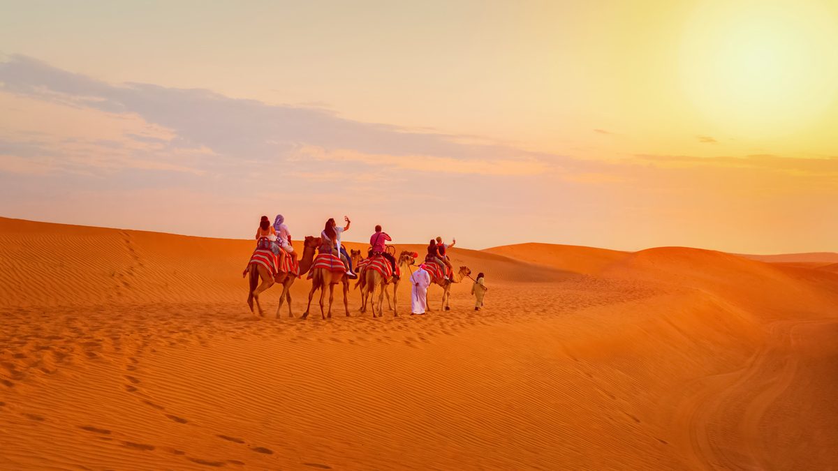 Travellers riding camels across desert dunes at sunrise near Dubai