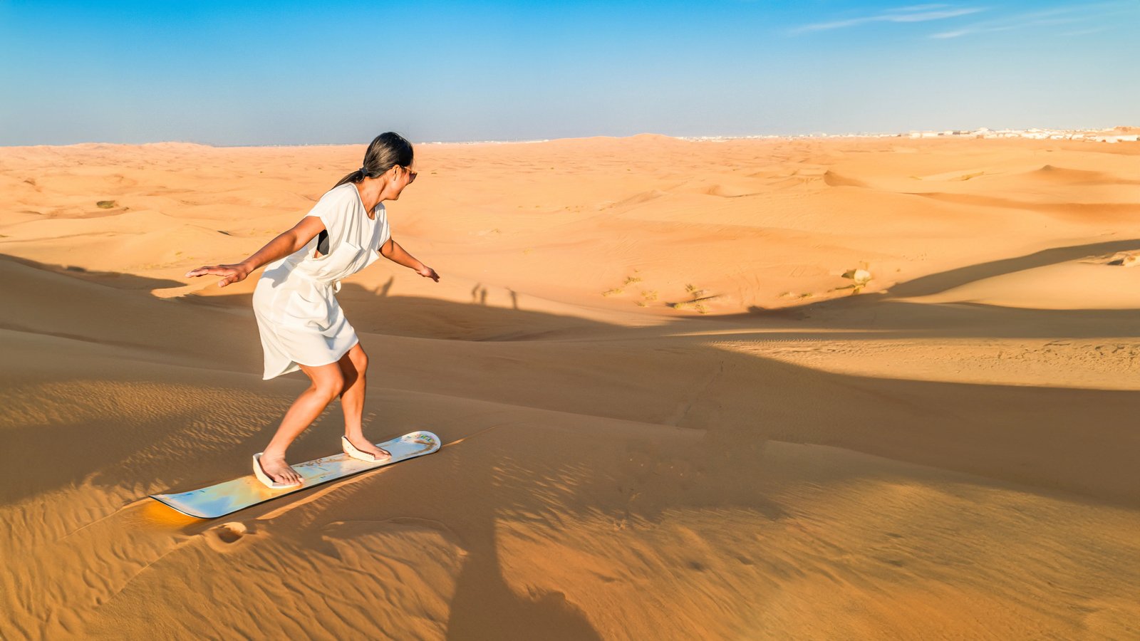 Woman sandboarding down a soft dune slope in the Dubai desert