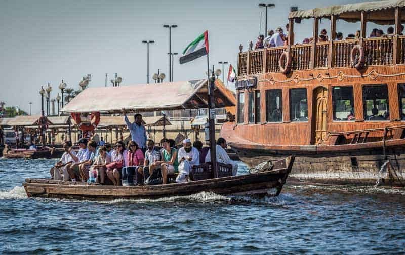 Tourists riding a traditional abra across Dubai Creek with a dhow behind