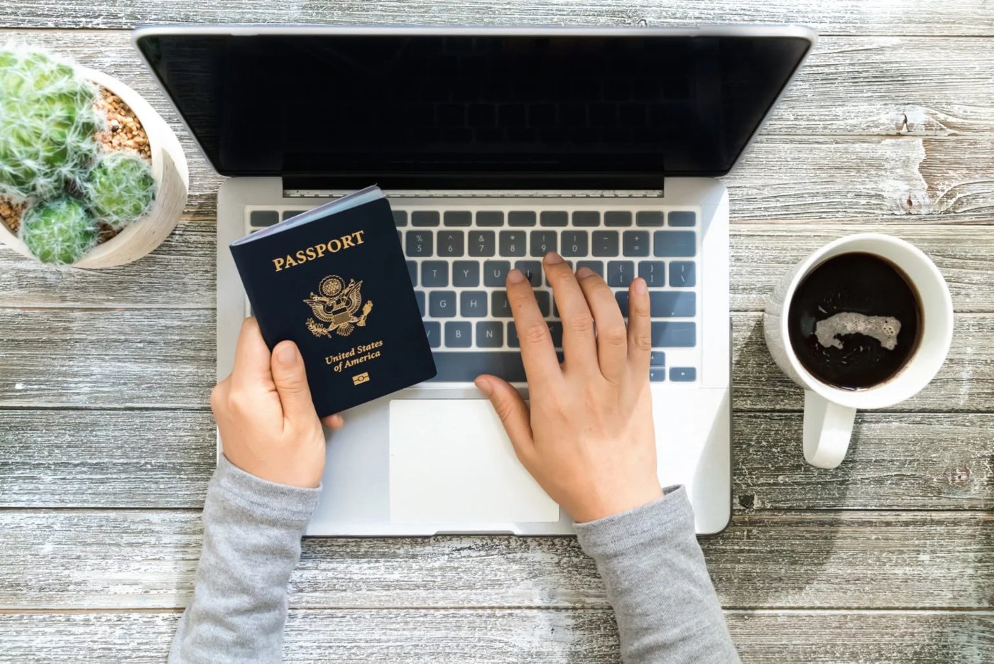 Person booking travel on a laptop with a passport beside the keyboard