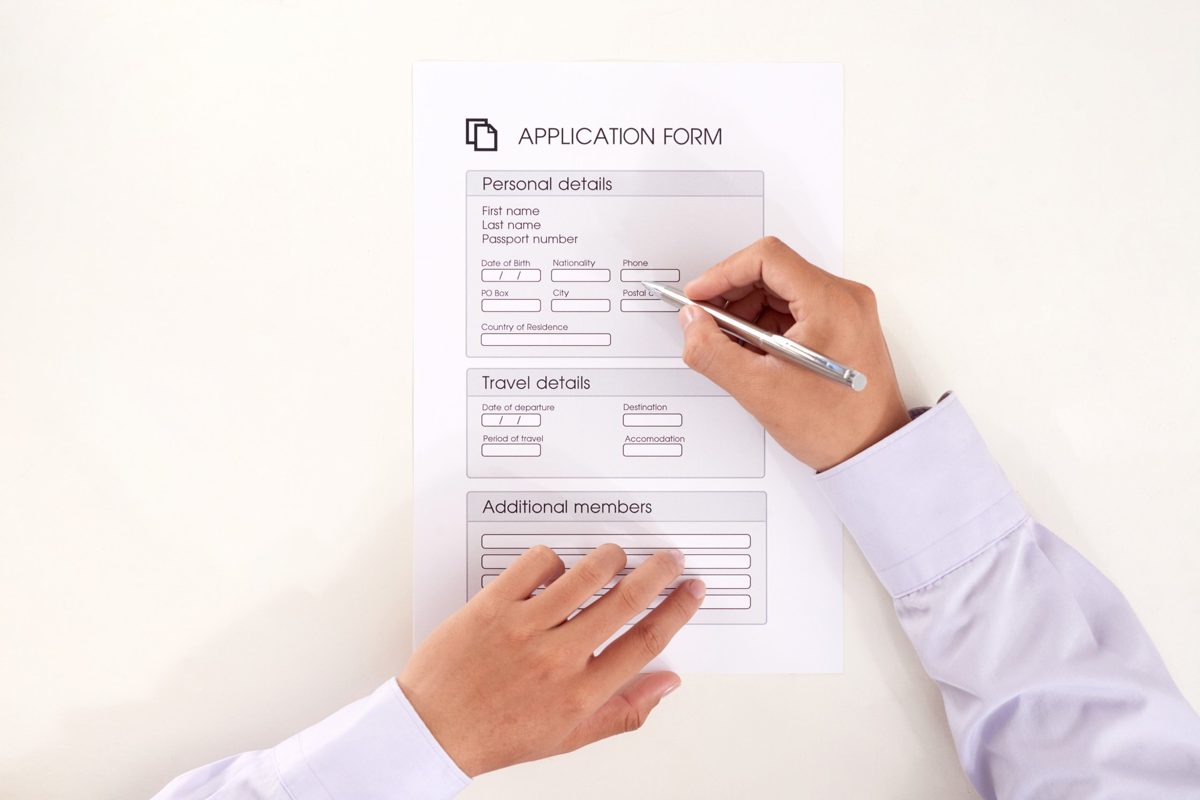 Someone completing a travel application form carefully with a pen