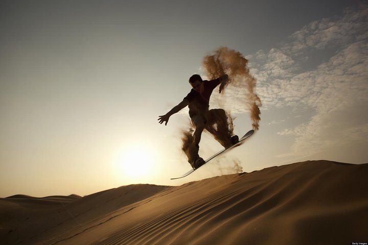 Tourist sandboarding down a tall dune in the Dubai desert