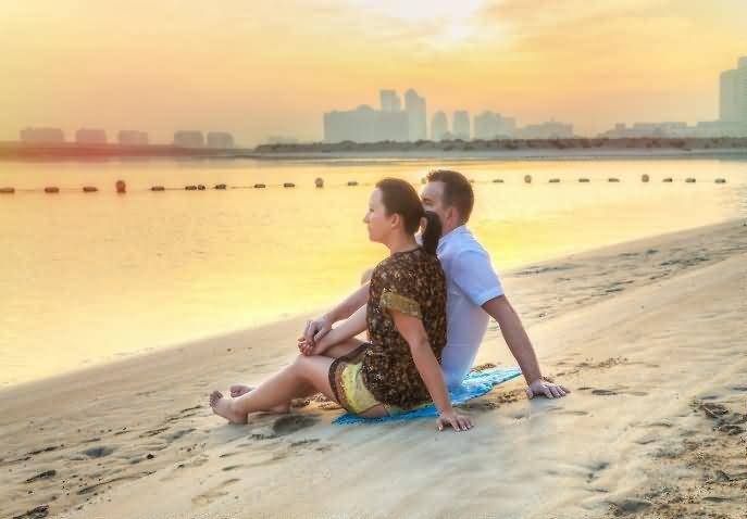 A couple sitting together on the sand watching the sunset over the Gulf